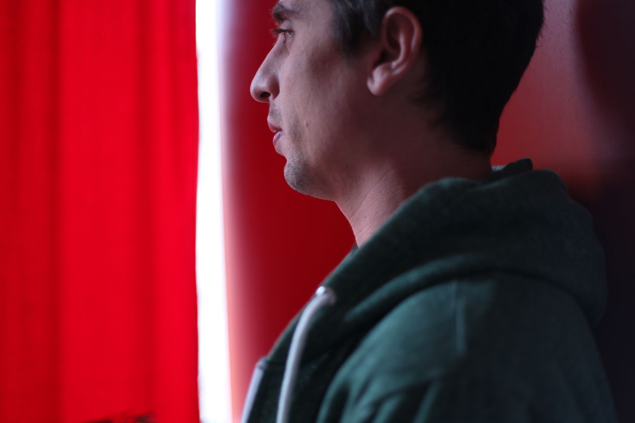 Close-up of thoughtful young man by red curtain