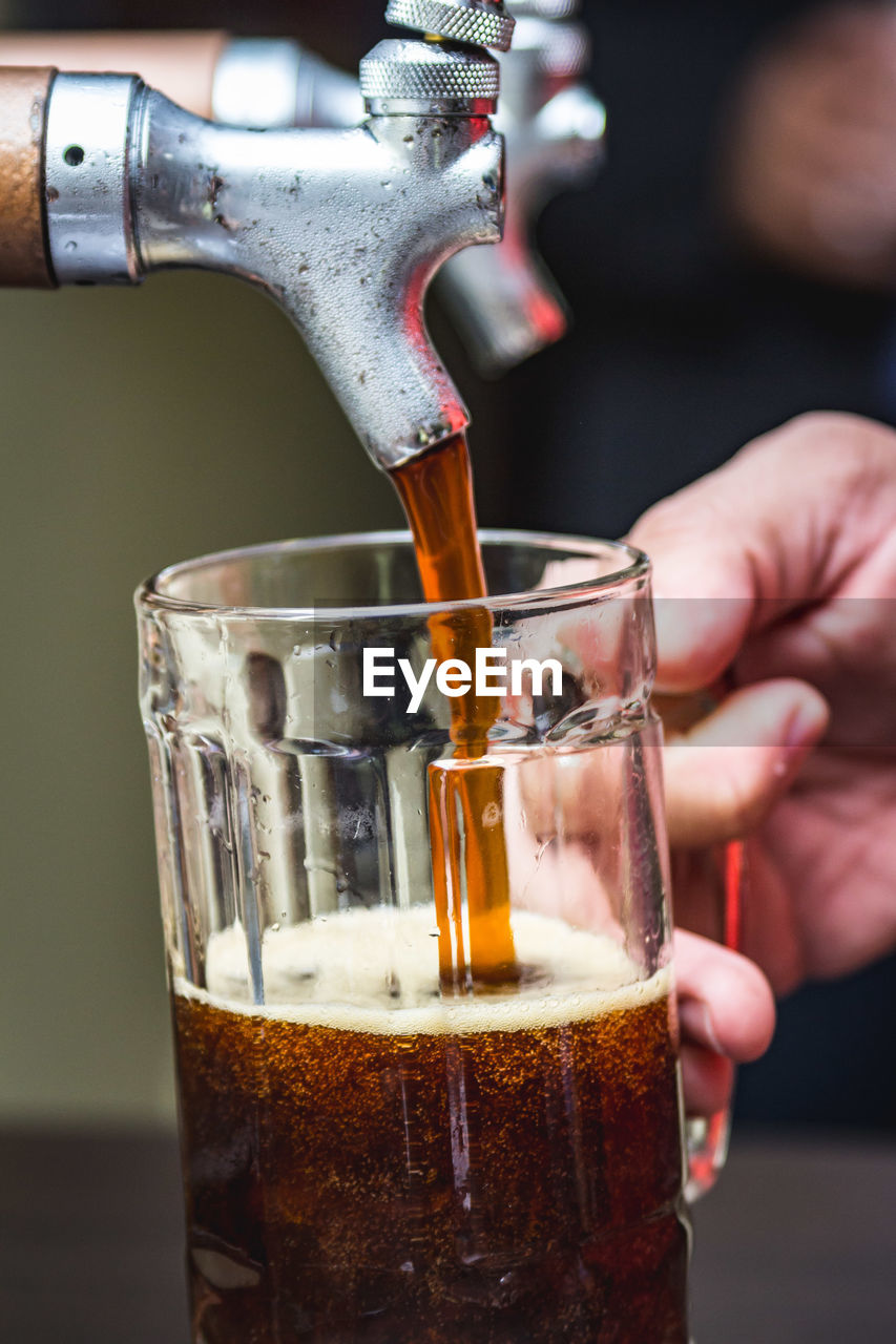 Close-up of cropped hands pouring beer in glass from tap
