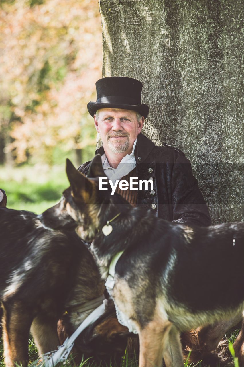 Portrait of man with dogs against tree trunk