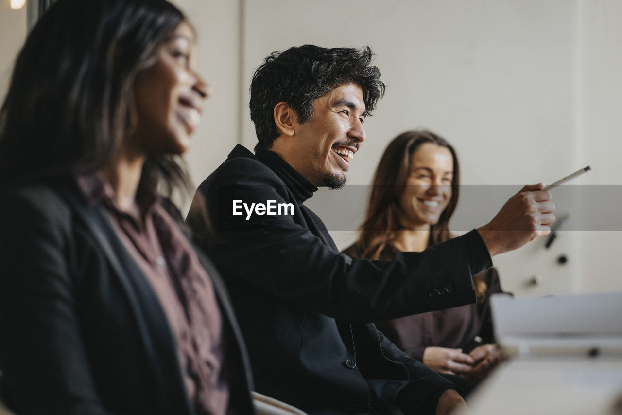 Happy male entrepreneur pointing during business meeting with female colleagues at office