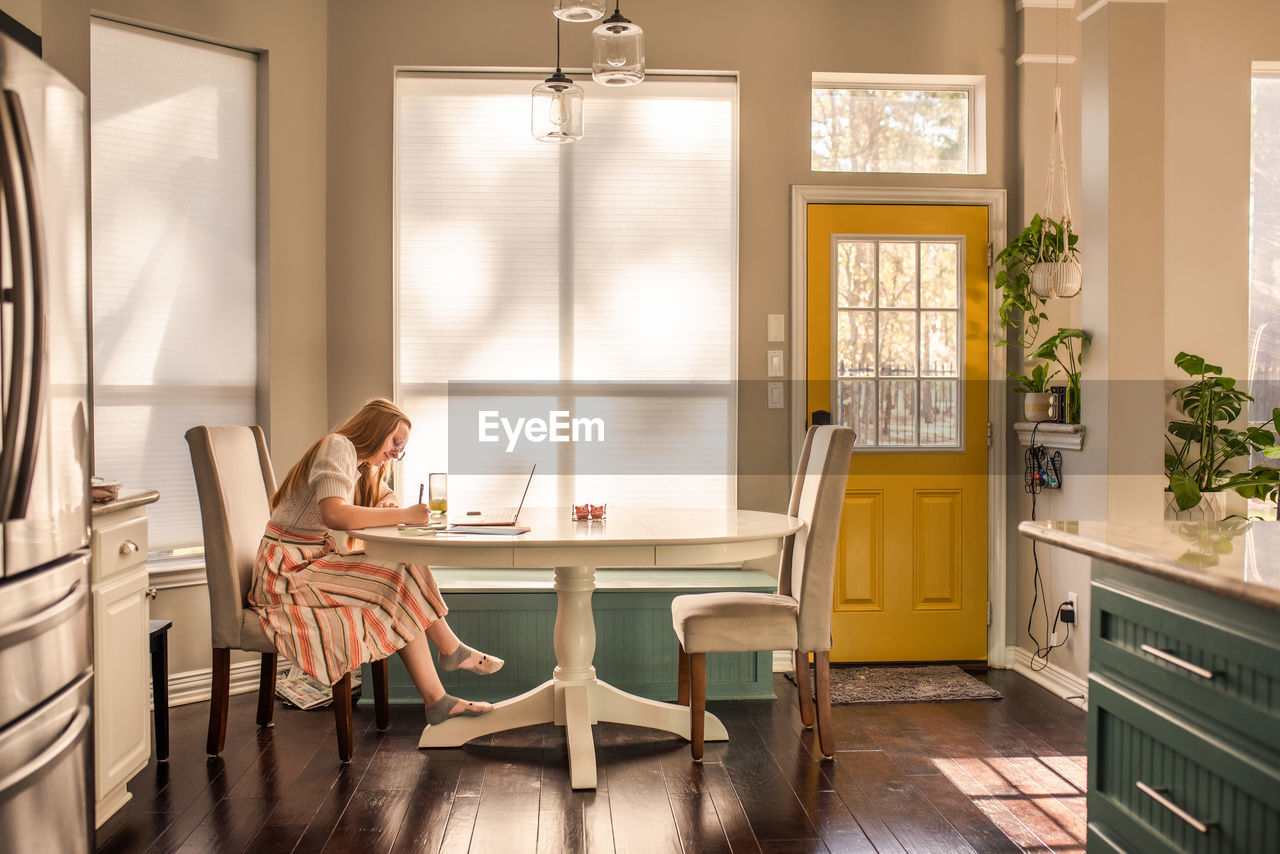 SIDE VIEW OF WOMAN SITTING ON TABLE IN ROOM