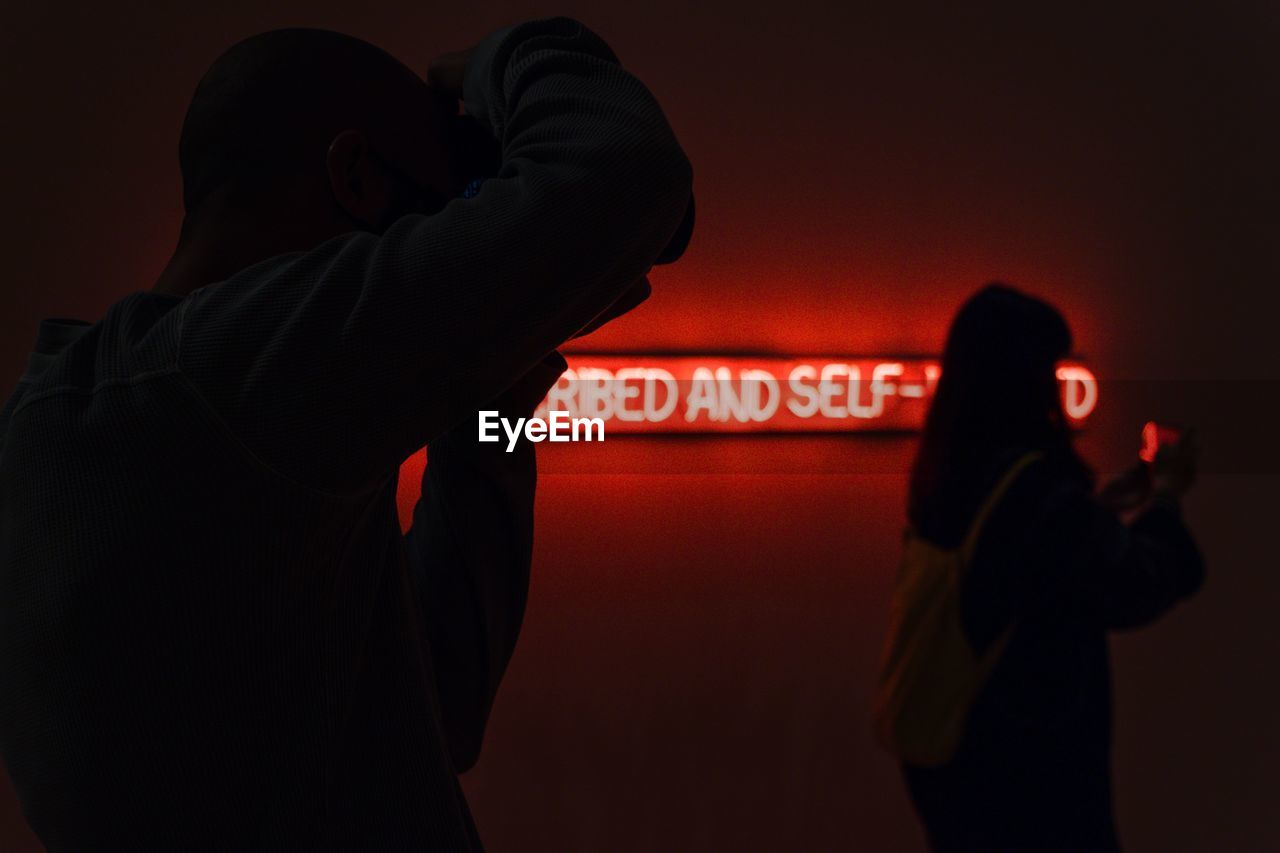 Rear view of man and woman standing against illuminated sign