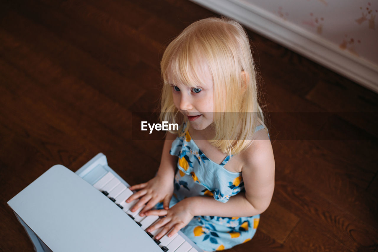 Little blonde girl plays a toy piano at home. musical development in childhood