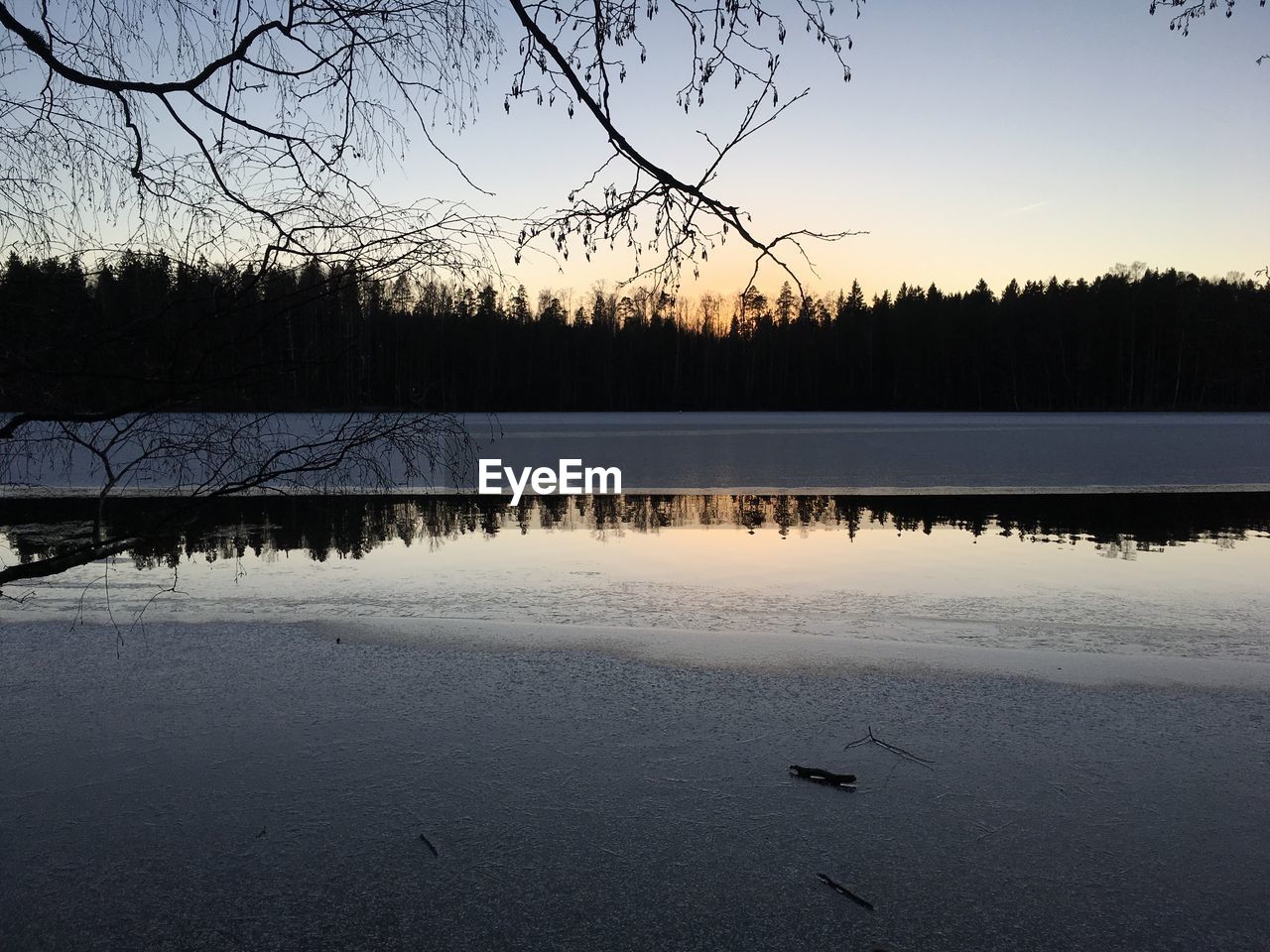 Sunset is reflected on water where melted area of frozen lake. 