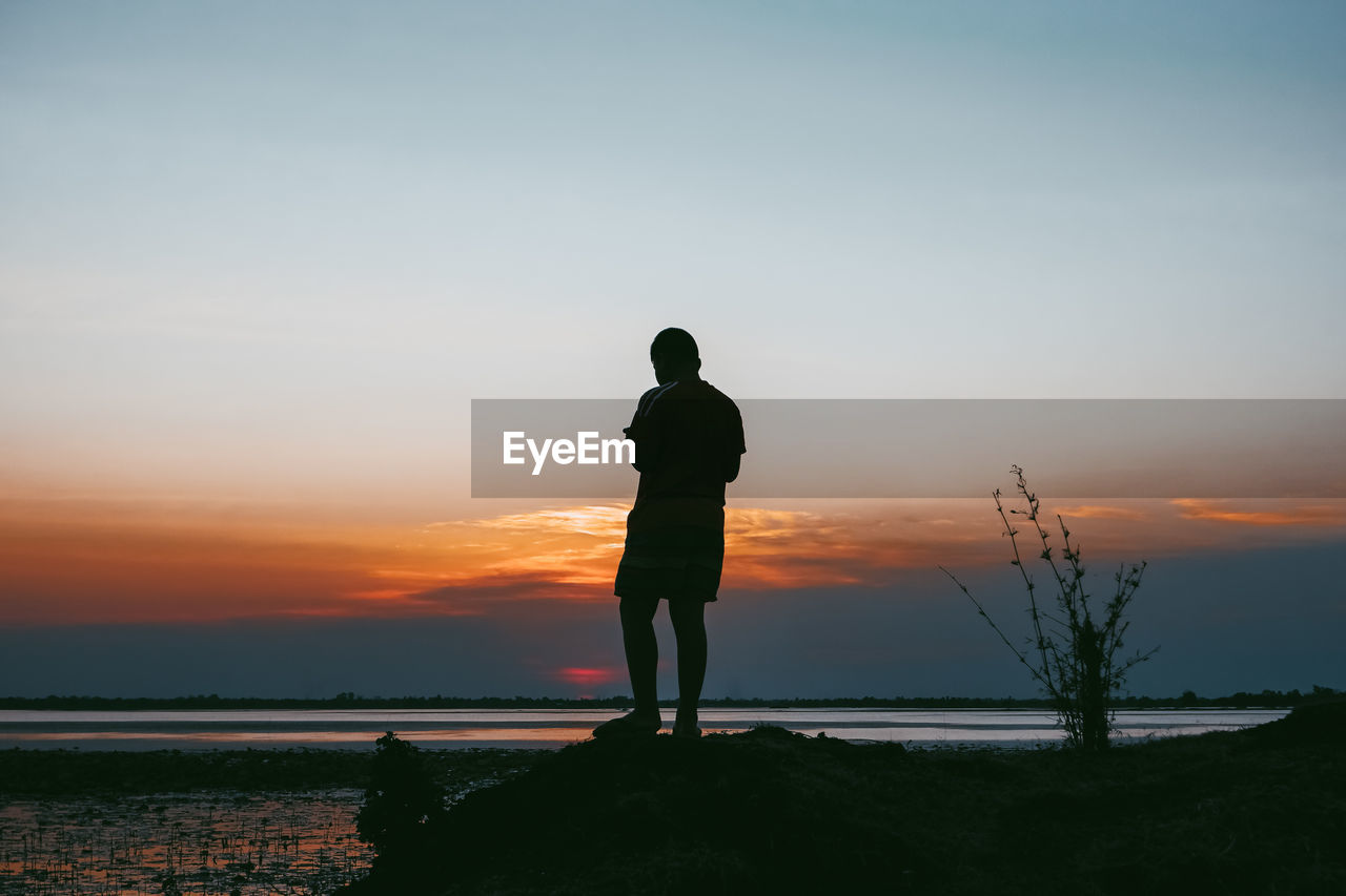 Rear view of silhouette man looking at sea against sky during sunset