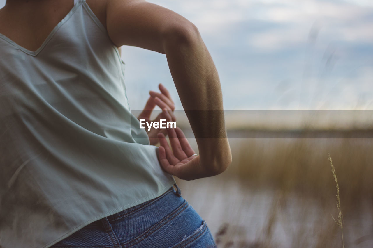 Midsection of young woman dancing against sky