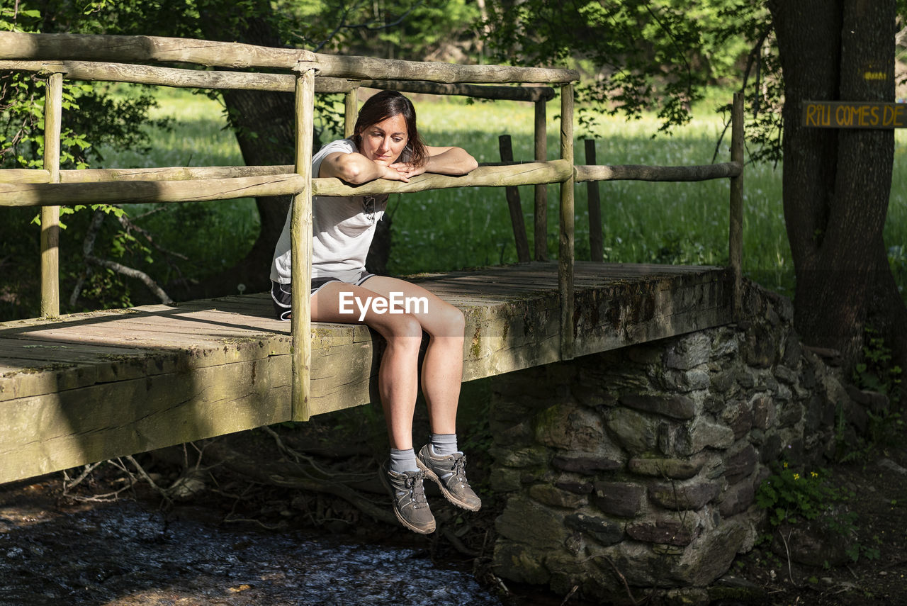 Fit woman sitting and relaxing on a wooden bridge in the middle