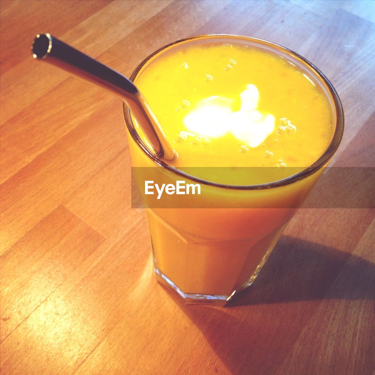 Close-up of fresh mango and orange smoothie with straw on table