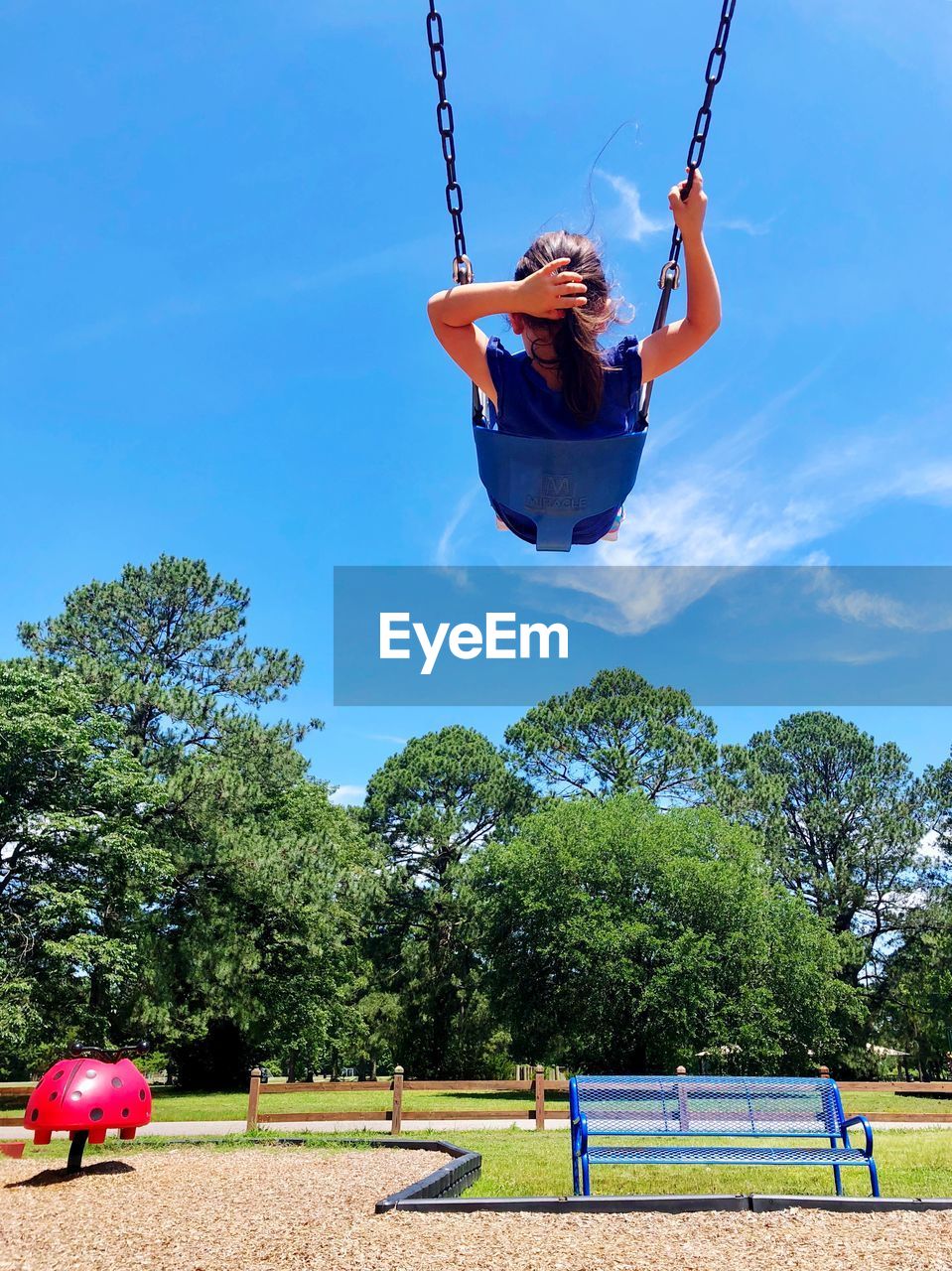 REAR VIEW OF WOMAN ON SWING IN PLAYGROUND