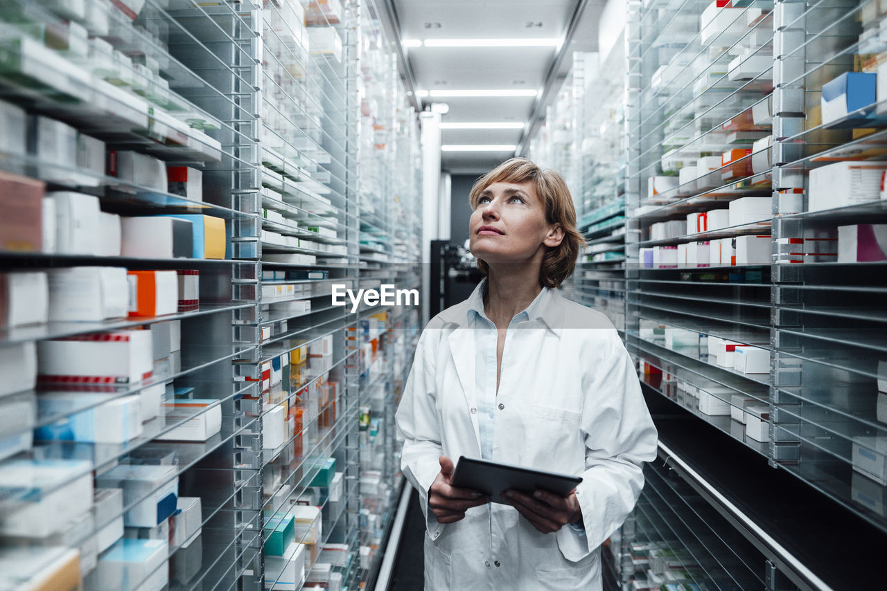 Female pharmacist looking at medicine while holding digital tablet at pharmacy store
