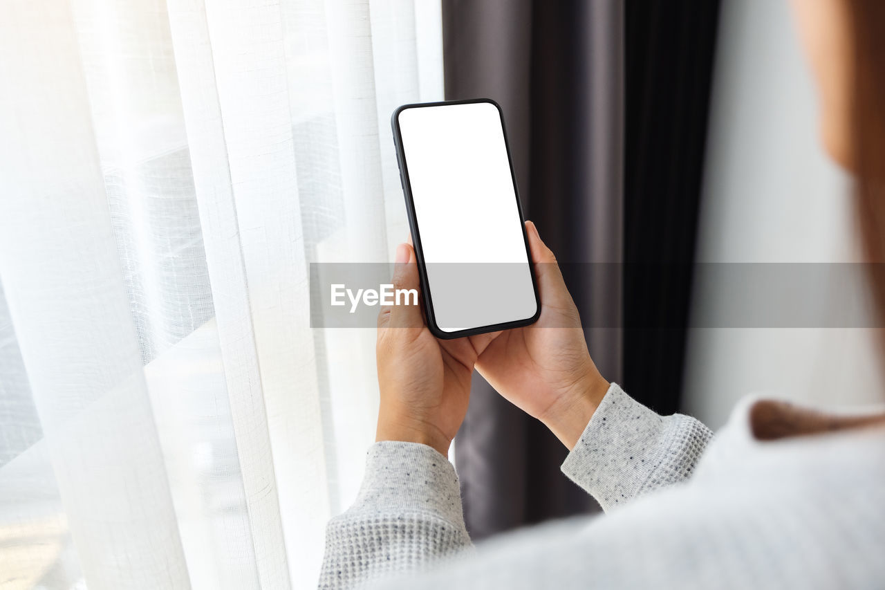 Mockup image of a woman holding mobile phone with blank white desktop screen