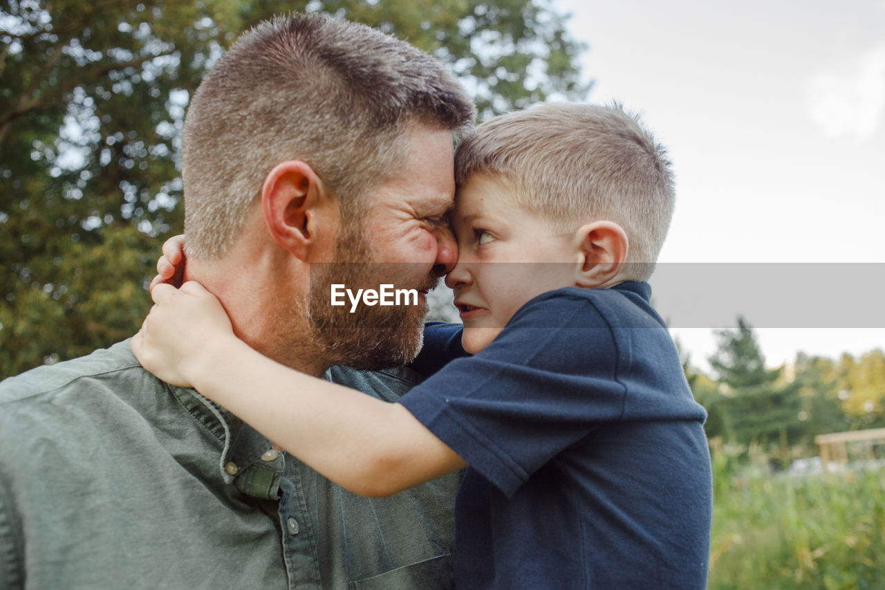 Close-up of playful father and son embracing while standing in forest