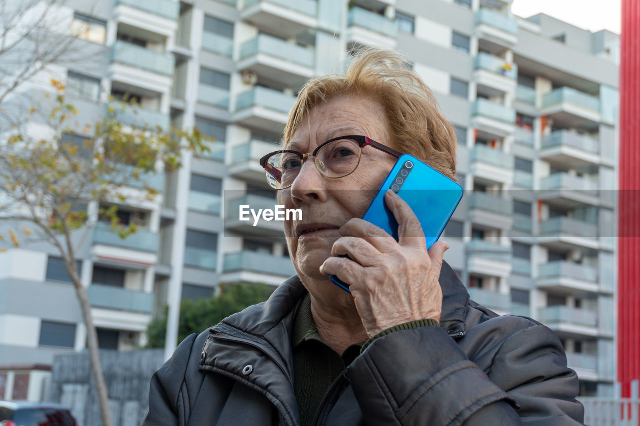 Portrait of a senior woman talking with a modern smartphone in the city streets.