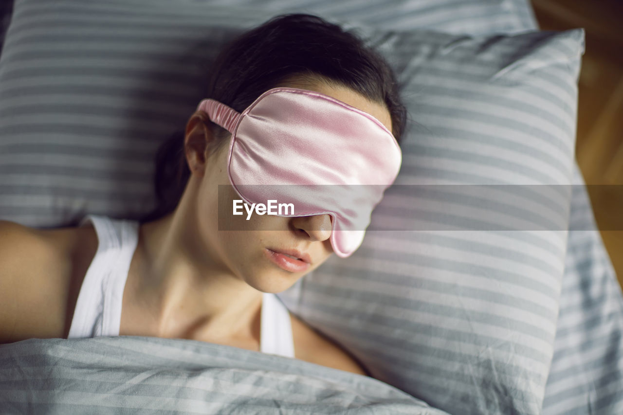 Woman in a pink eye mask lies under a blanket in a bed and suffers from insomnia