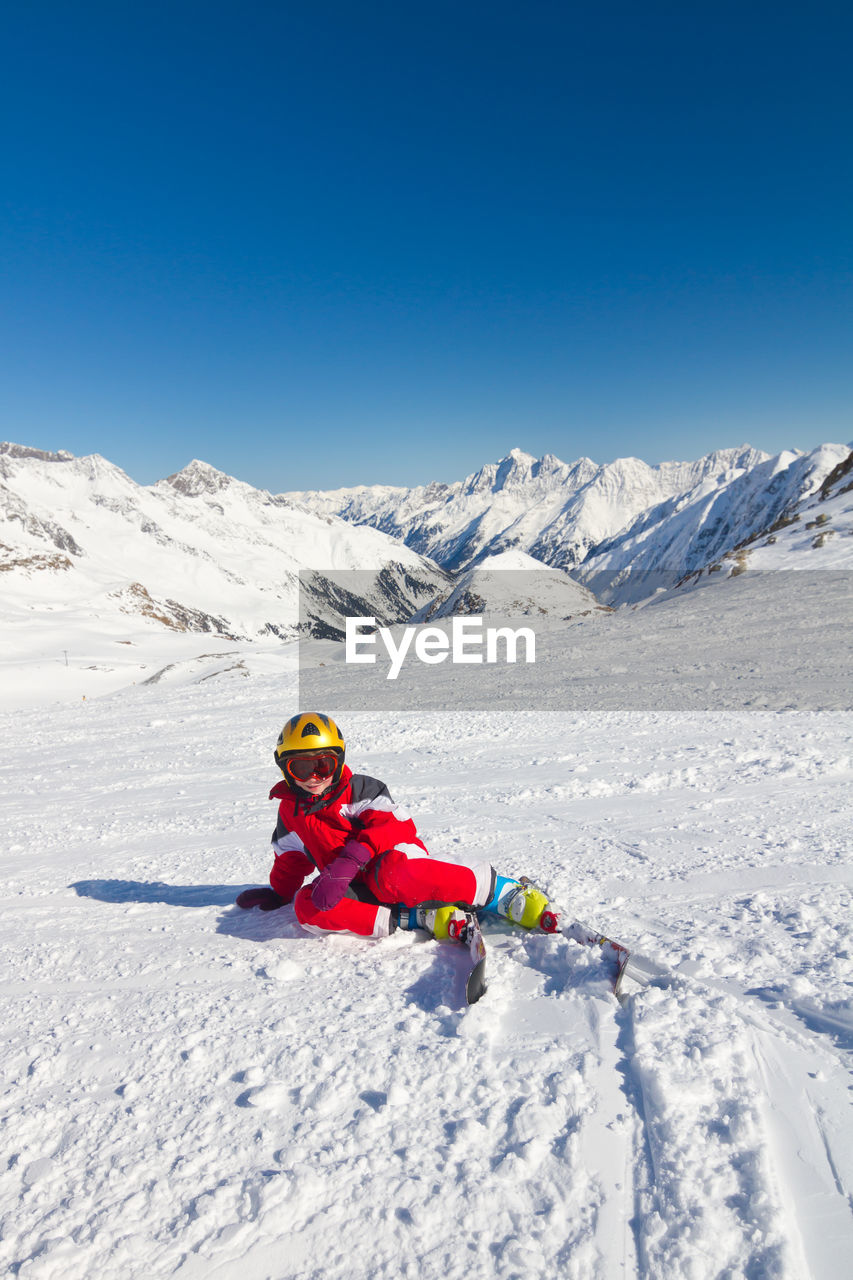 Girl skier sitting and resting on a ski slope in high mountains