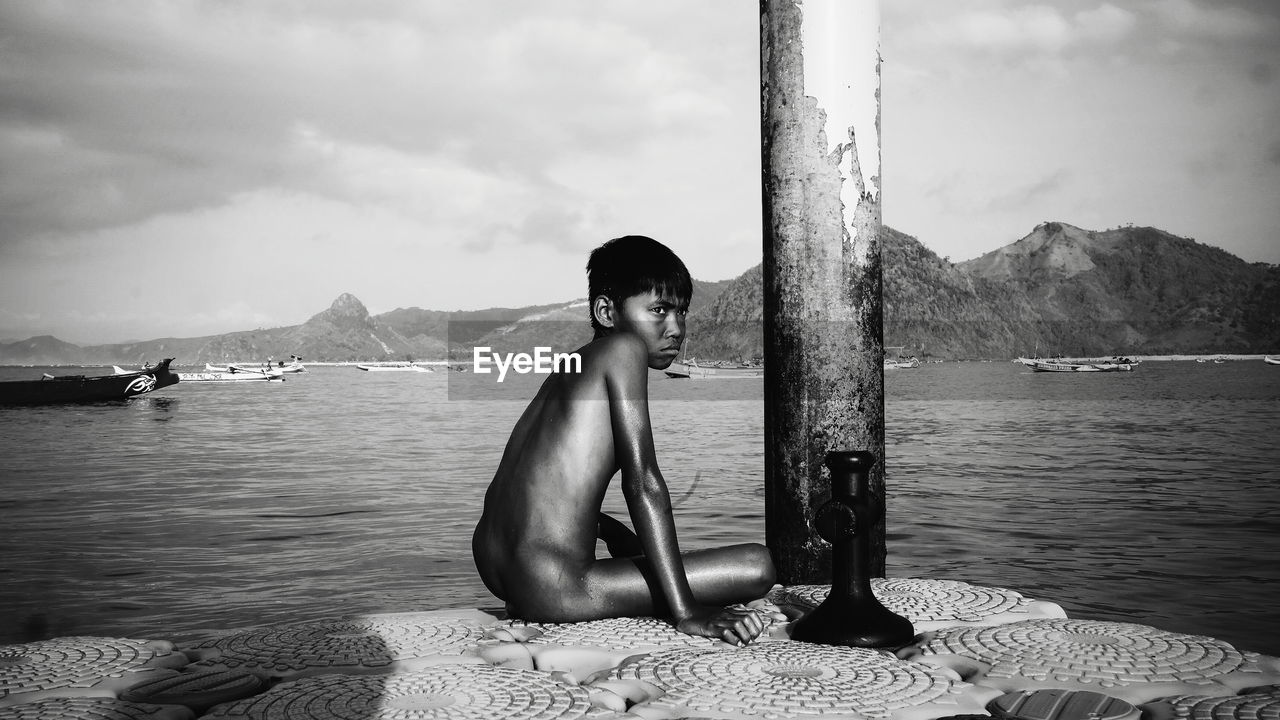 MAN SITTING IN SEA AGAINST SKY