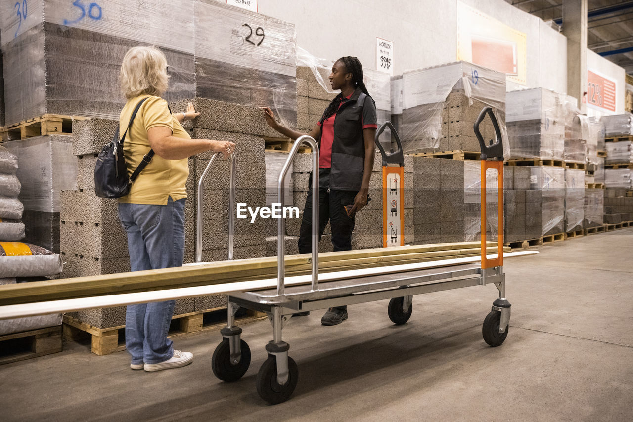 Female customer near cart talking with sales staff at hardware store