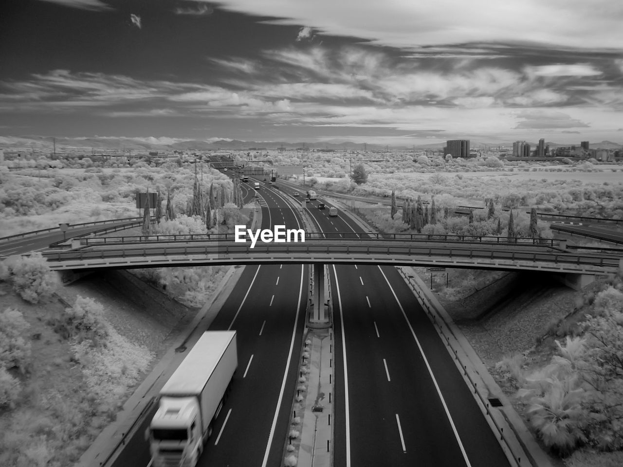 Infrared image of bridge over road against cloudy sky