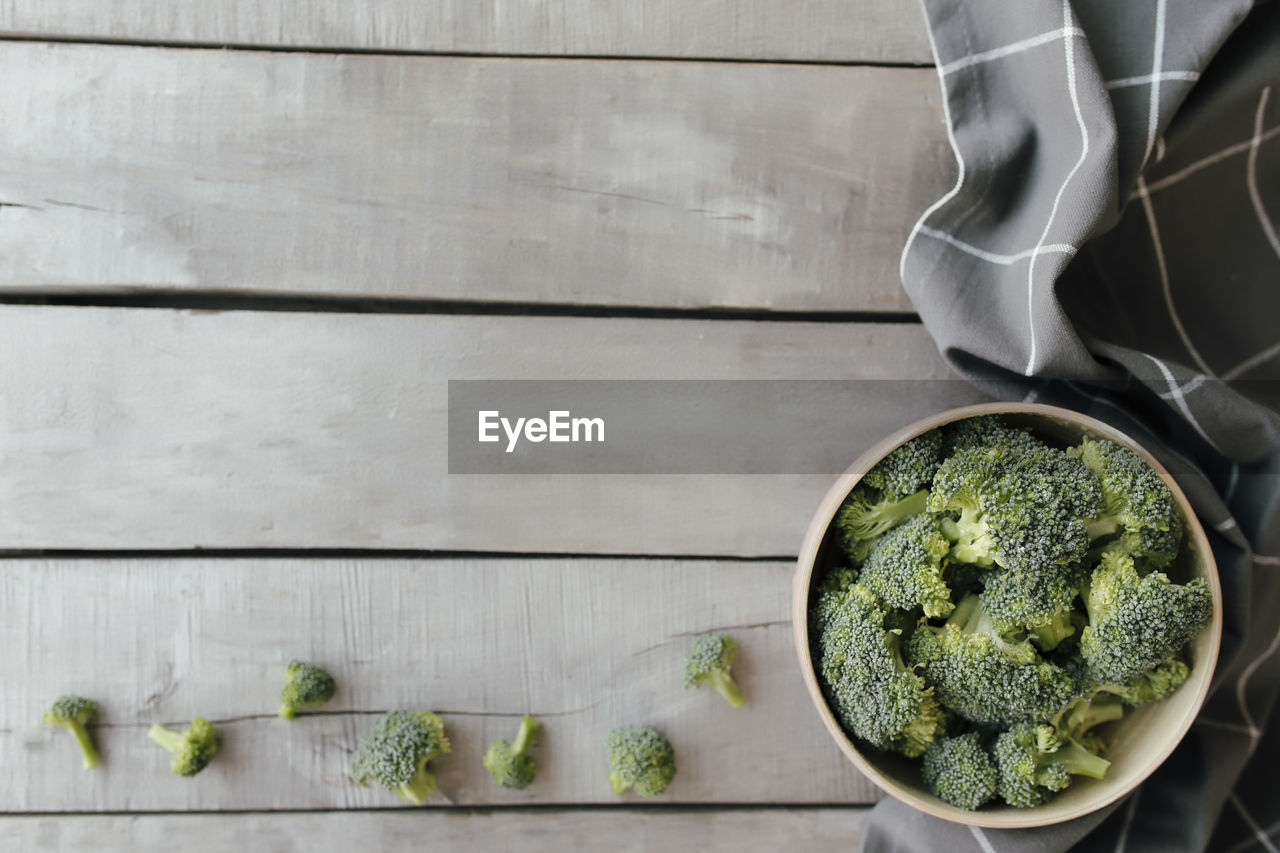 Green fresh broccoli in bowl on wooden background, gray towel. healthy eating concept