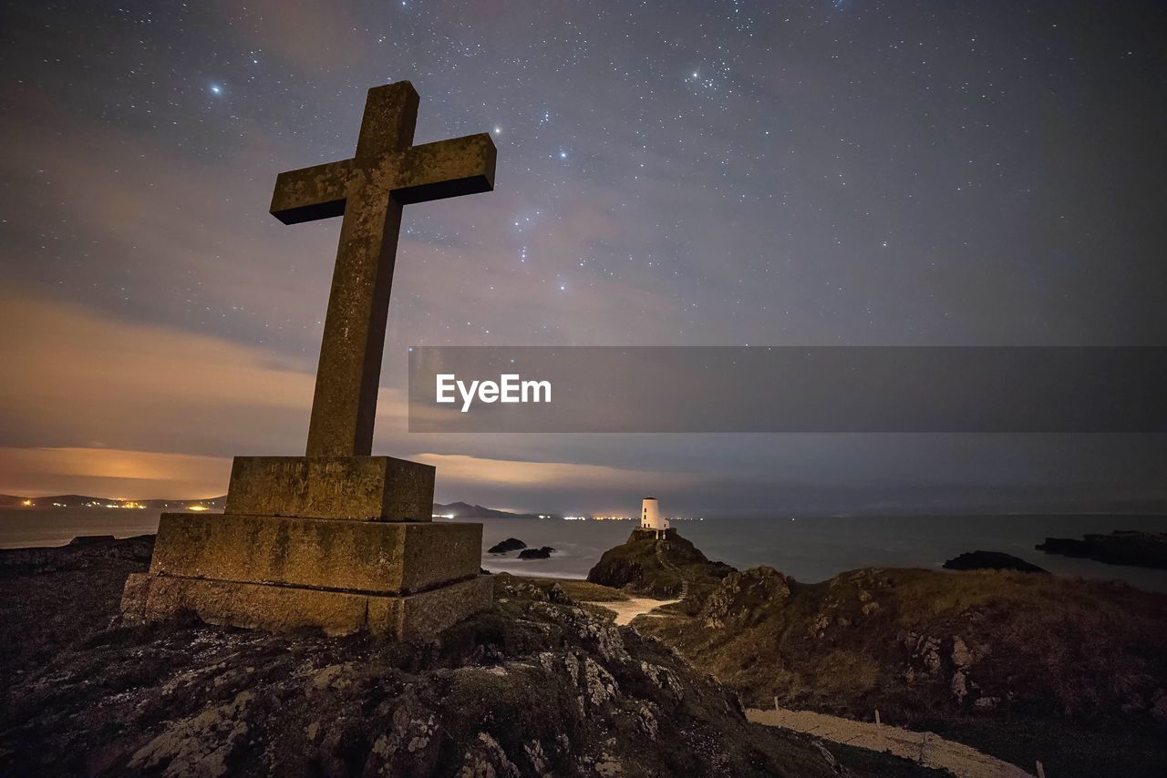 Low angle view of cross at sea shore against sky