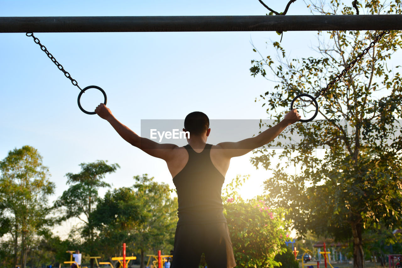 Rear view of man exercising with gymnastic rings against sky
