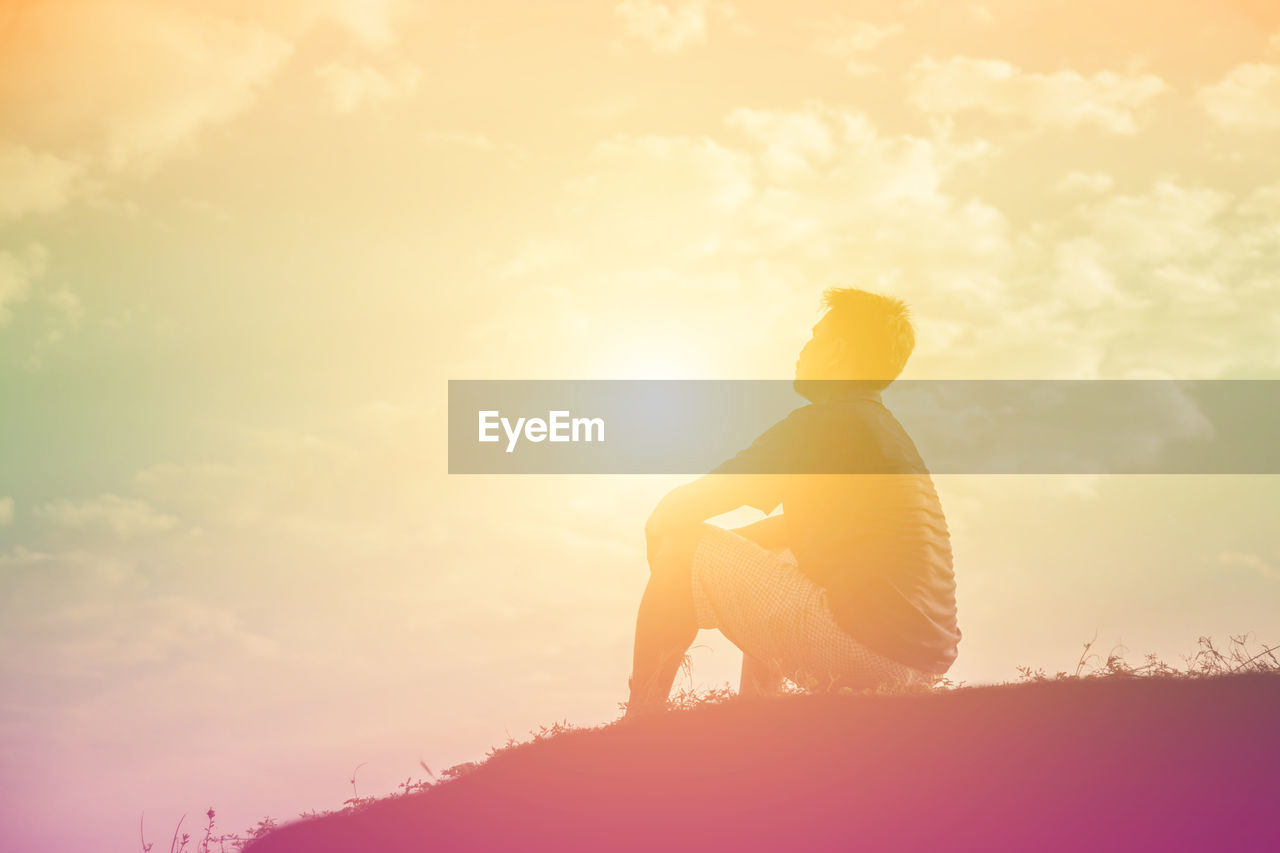 Side view of silhouette man sitting on land against sky during sunset