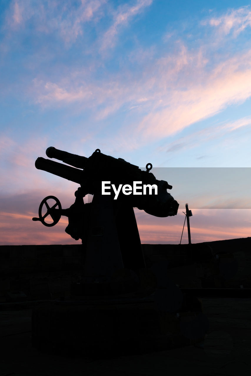 Silhouette weapon against sky during sunset