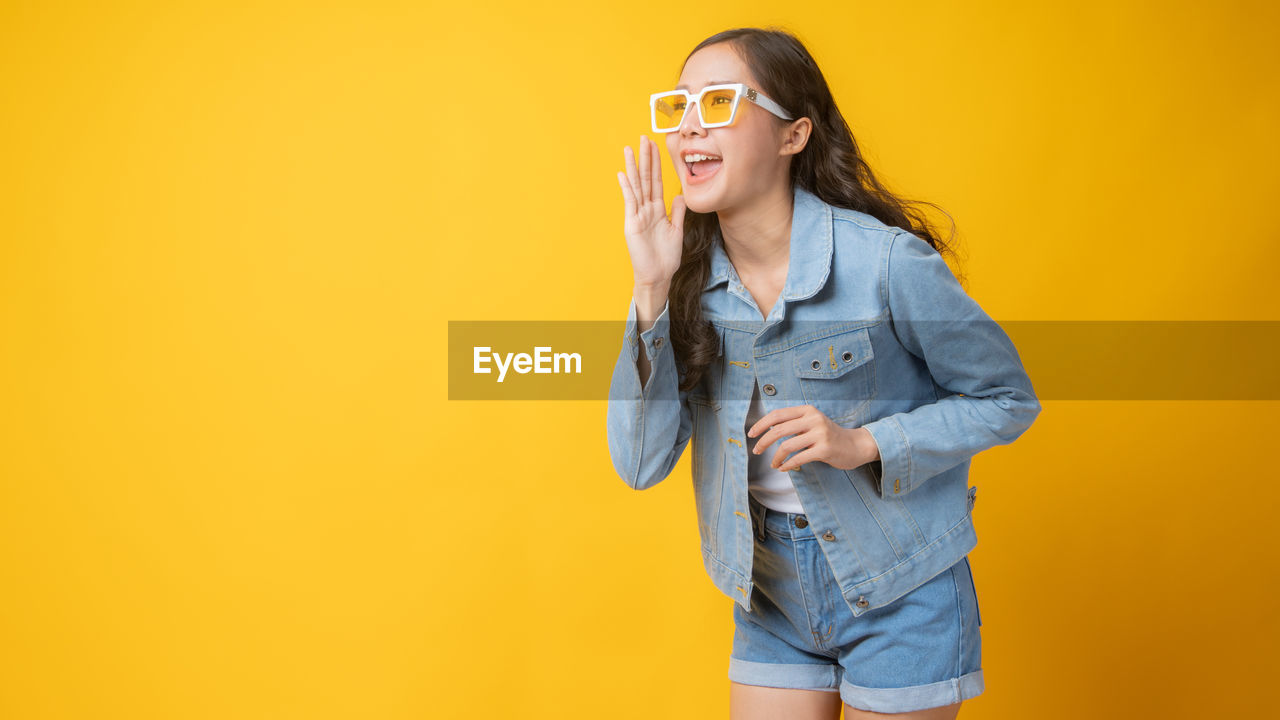 YOUNG WOMAN WEARING MASK AGAINST YELLOW BACKGROUND AGAINST ORANGE WALL