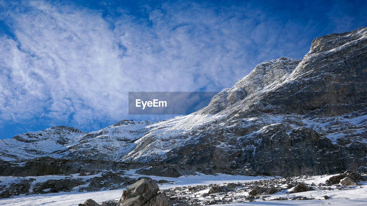 Scenic view of snowcapped mountains against blue sky with patchy  white cloud.