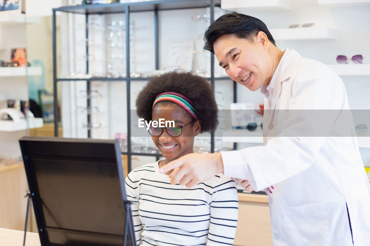 Man professional optician selling and young woman african american choosing spectacles glasses.