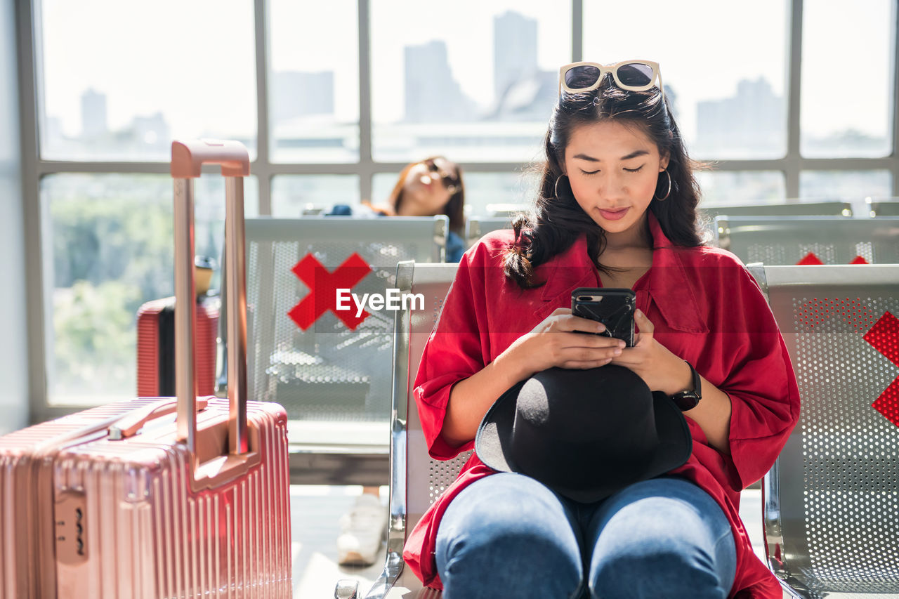 Young woman using mobile phone while sitting at airport