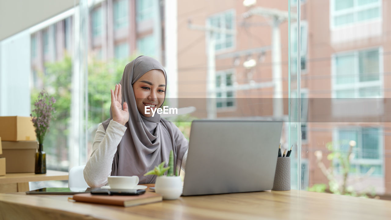 portrait of young woman using mobile phone while sitting on table in office