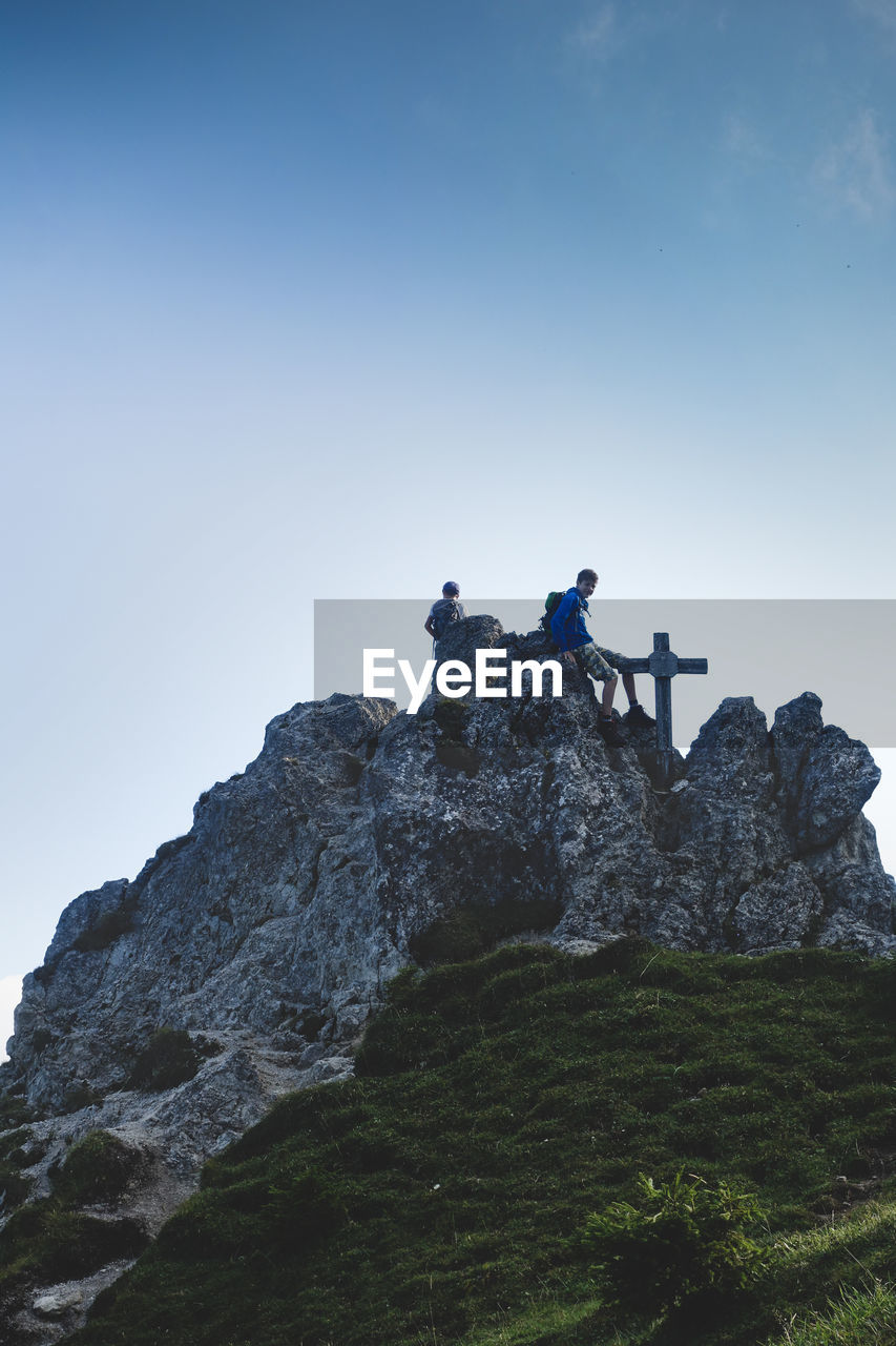 Low angle view of boys on rock against clear sky