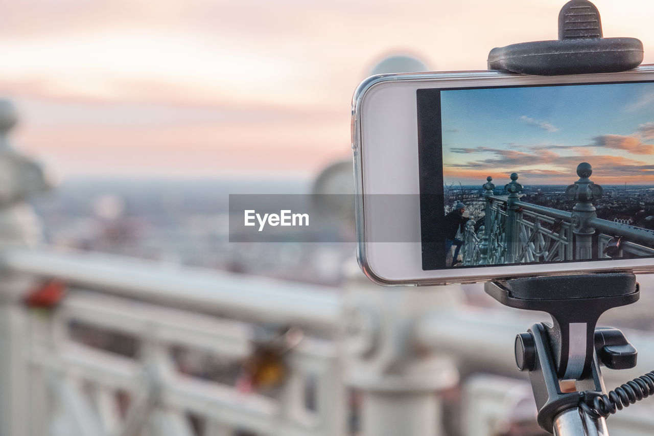 Close-up of smart phone in city against sky during sunset