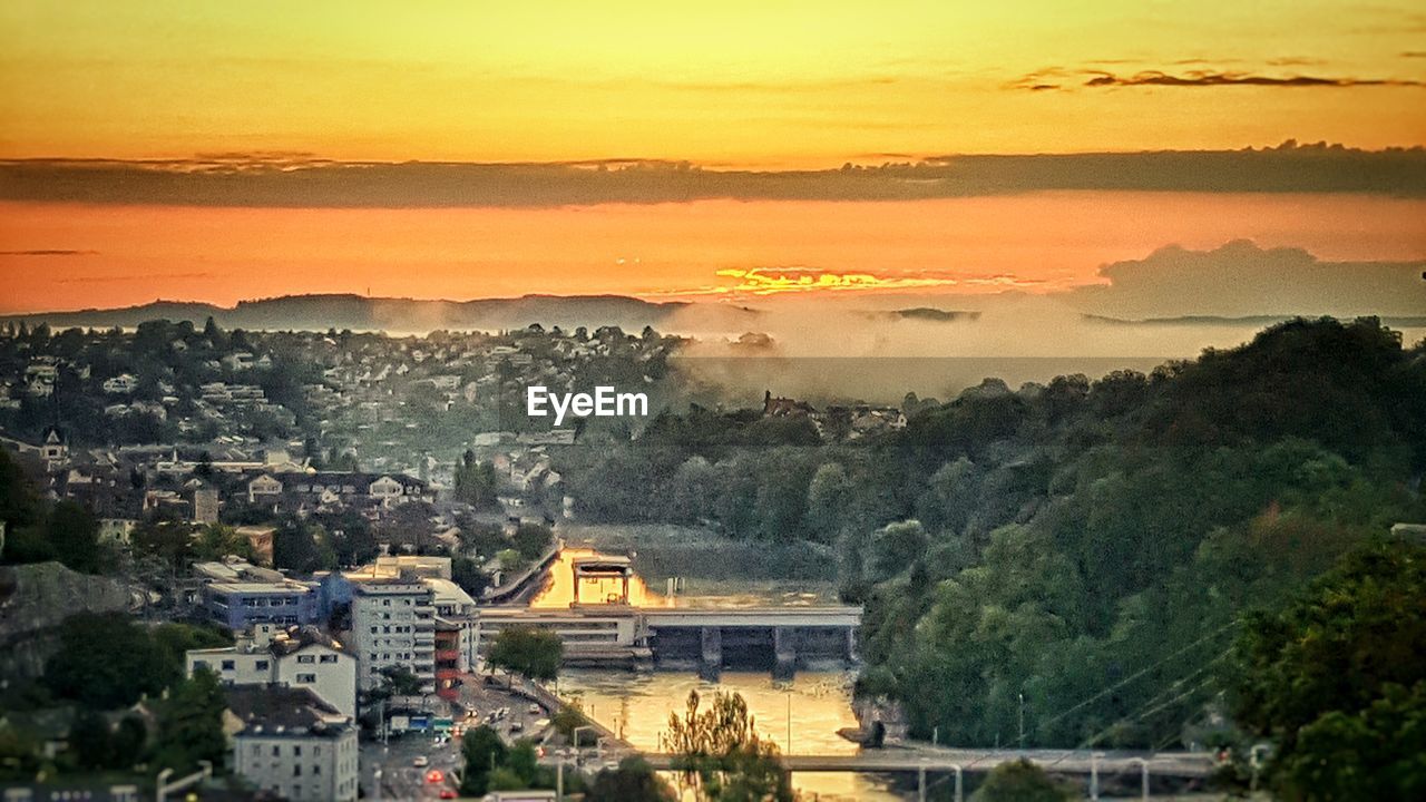 AERIAL VIEW OF TOWNSCAPE BY SEA AGAINST SKY DURING SUNSET