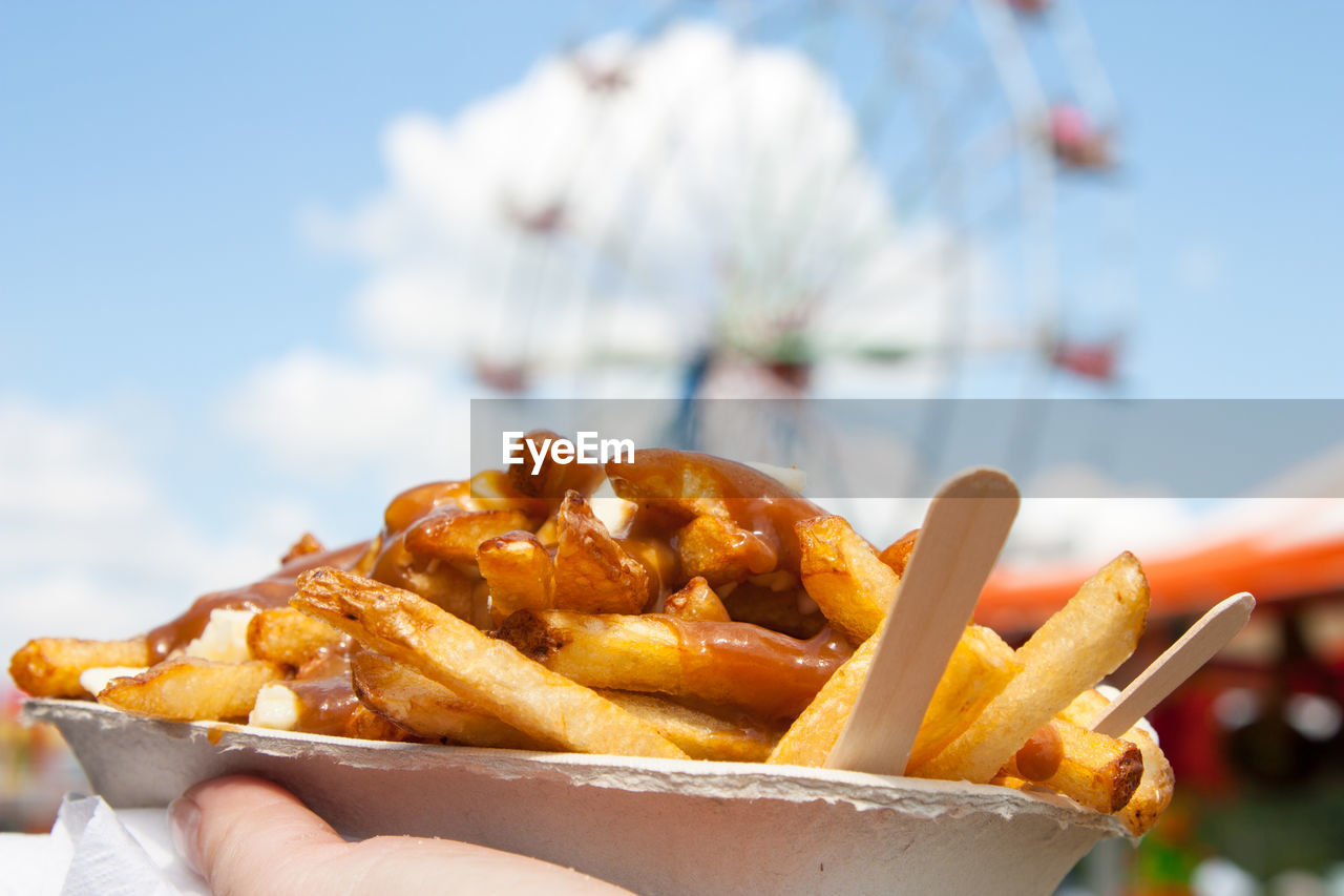 Cropped hand holding french fries against ferris wheel