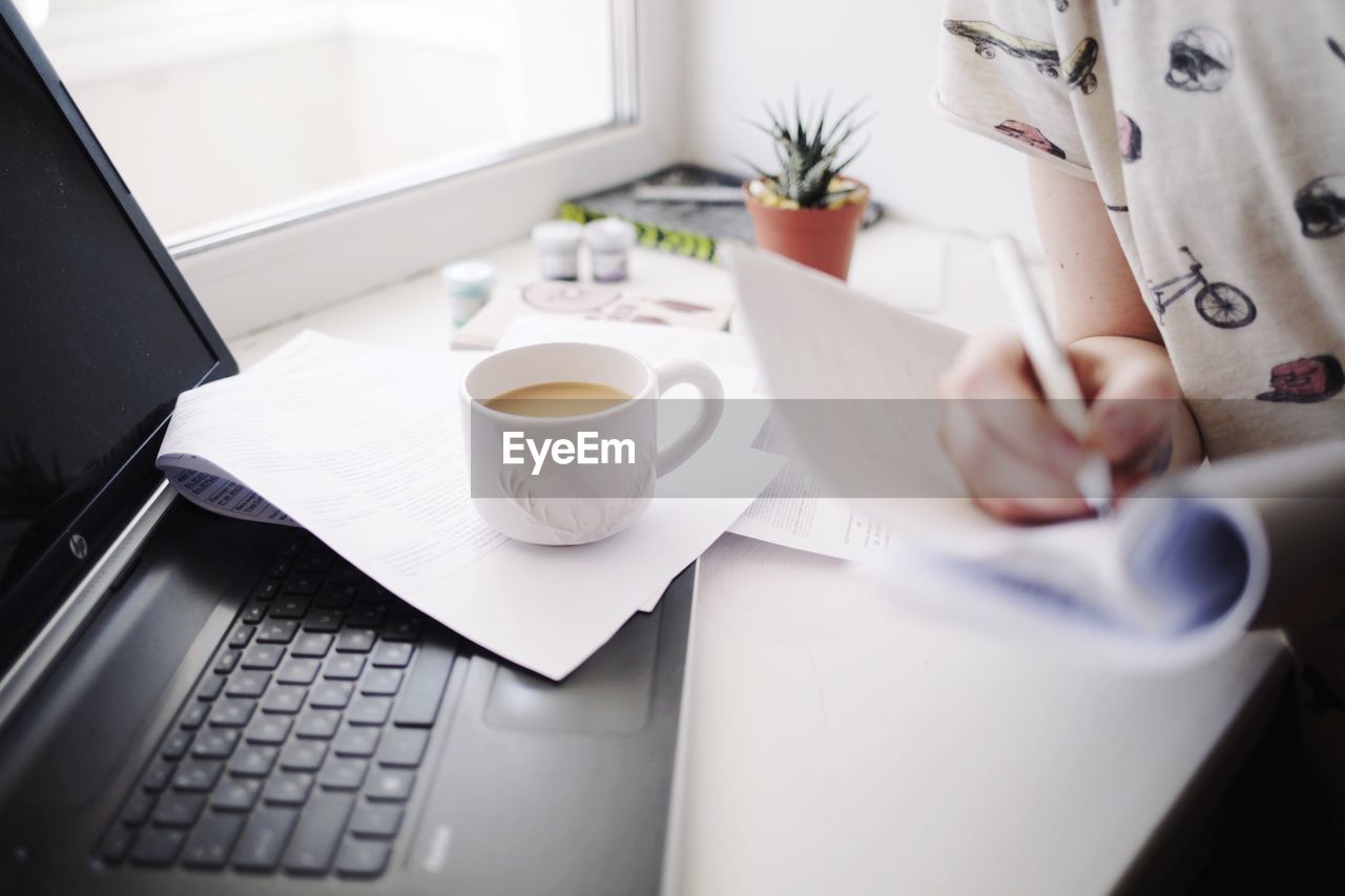 Midsection of woman working with coffee cup on table