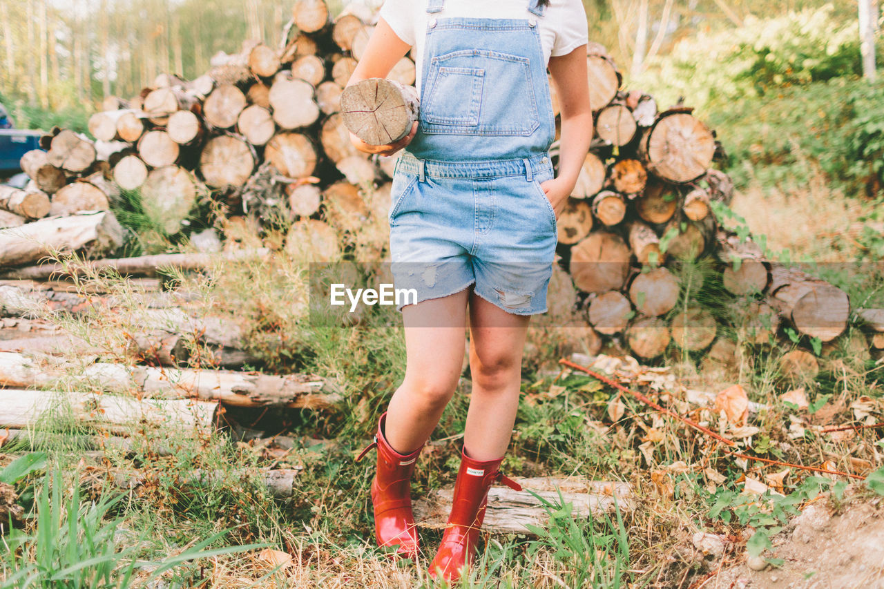 Low section of girl carrying log while standing on field