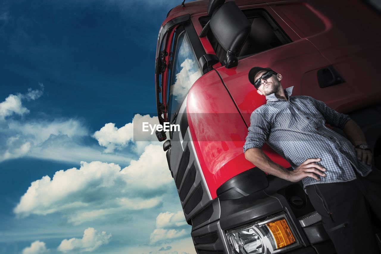 Low angle view of man standing by truck against cloudy sky