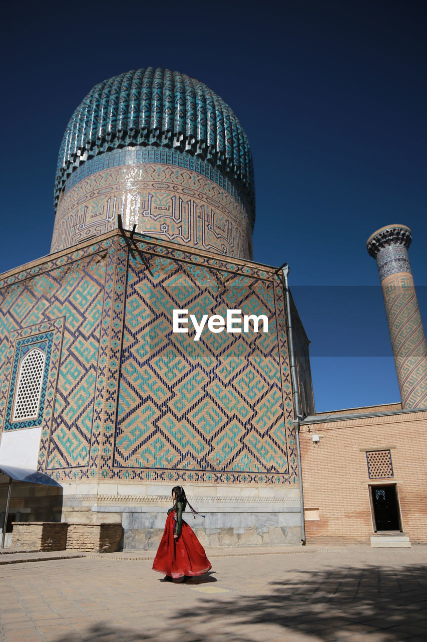 Woman walking by building against sky