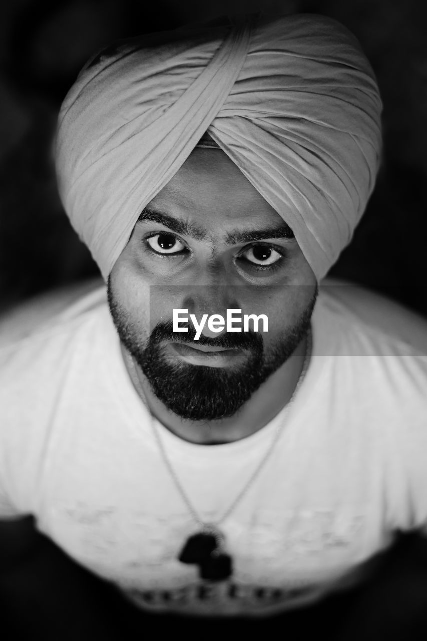 High angle portrait of young man wearing turban over black background