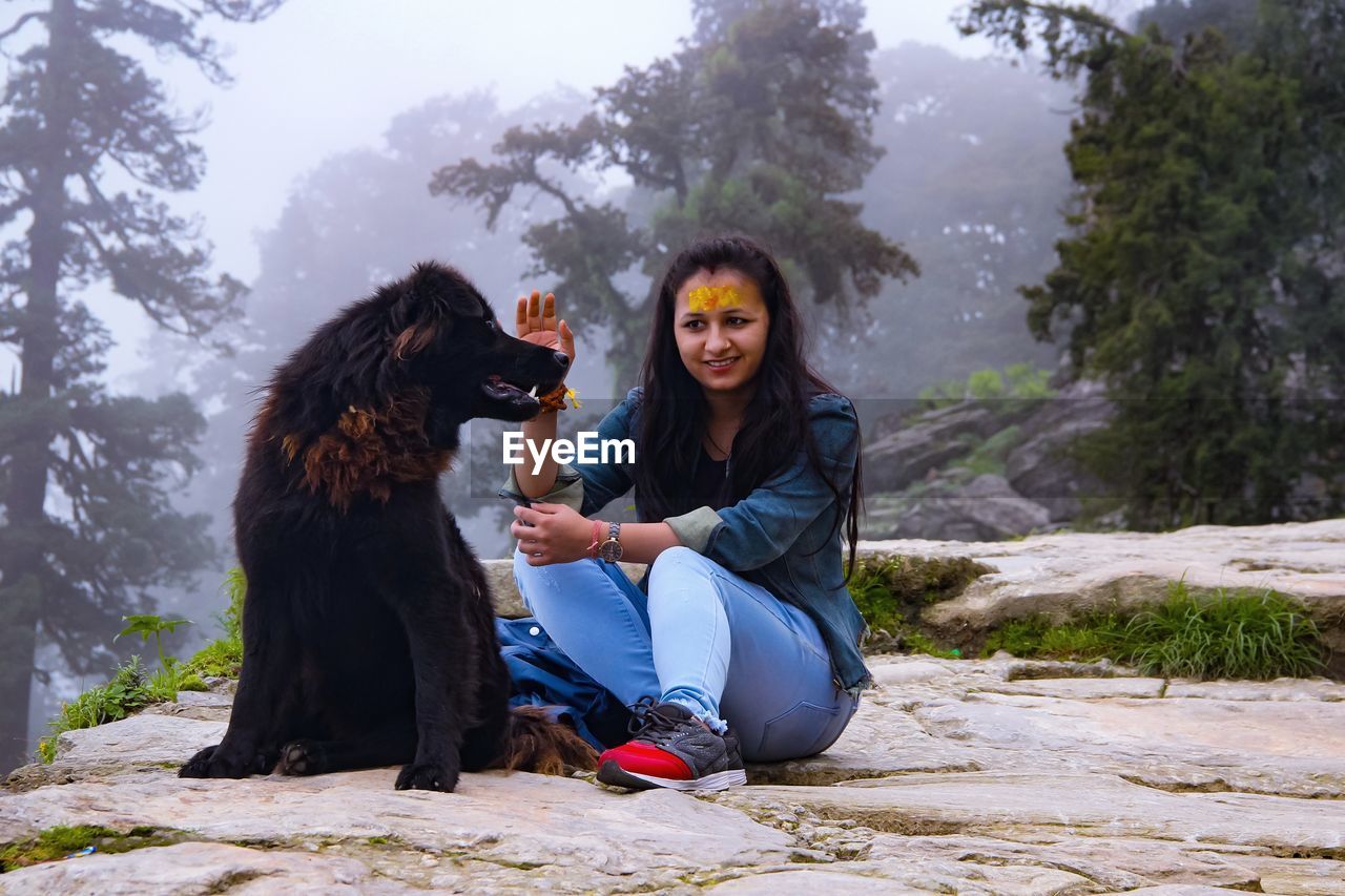 Full length of woman sitting dog against trees