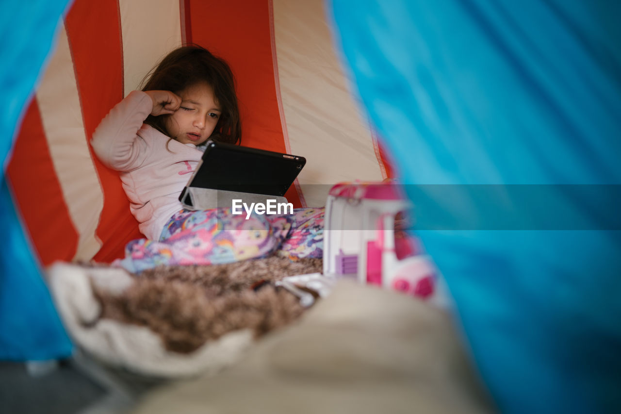 Four-year-old girl in pajamas looking at tablet in a little house