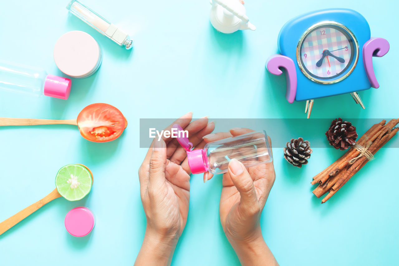 Cropped image of woman applying hand sanitizer by personal accessories over colored background