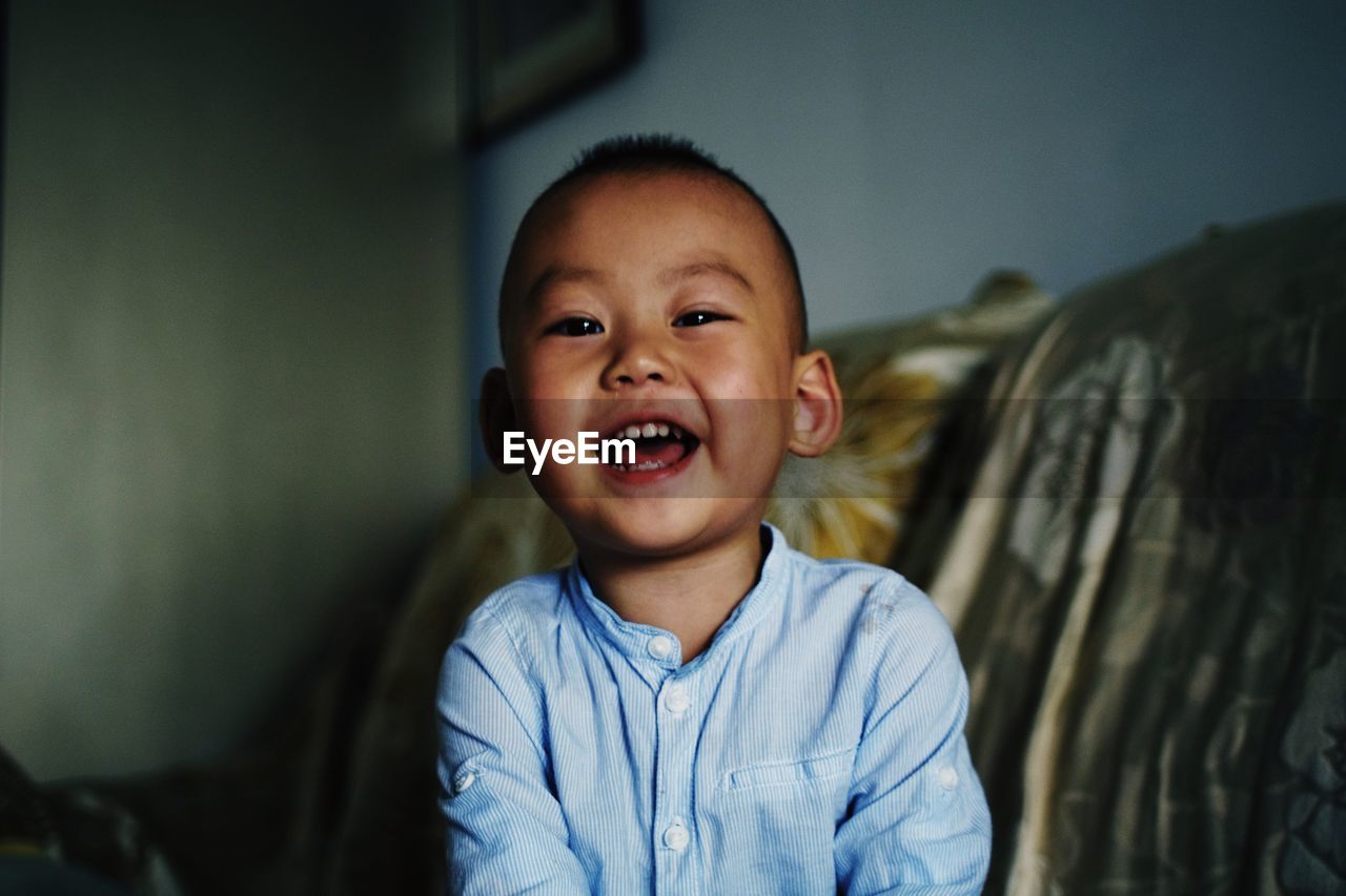 Portrait of cute cheerful boy sitting on sofa at home