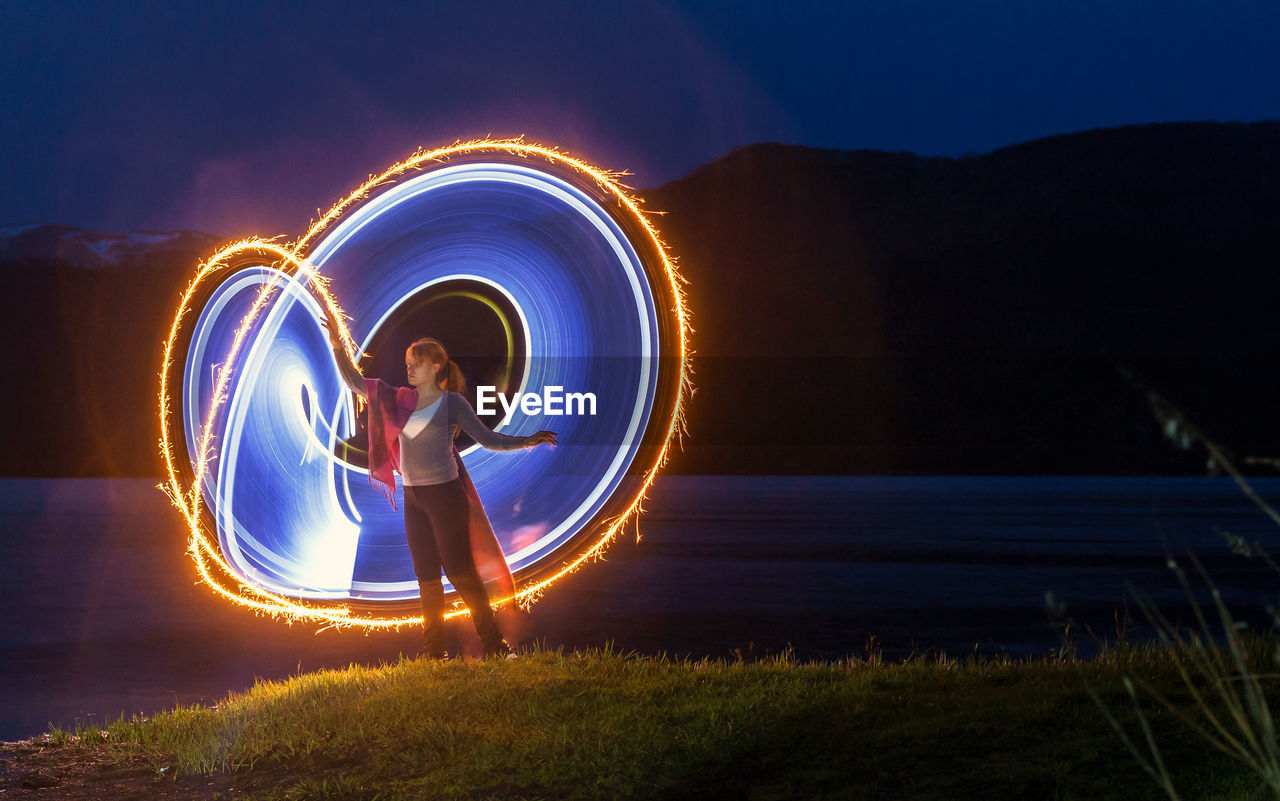 Woman making lighting paintings by lake at night