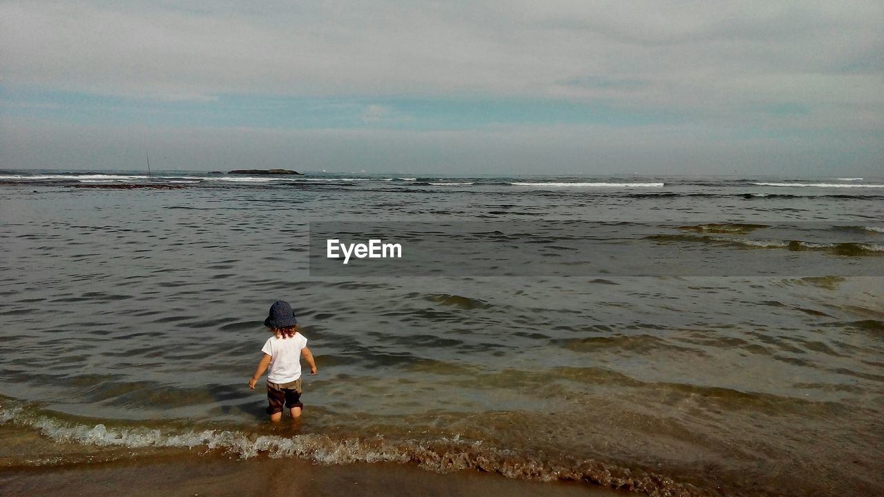 Rear view of kid in standing on shore against sky