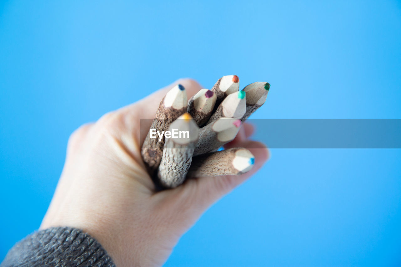 Cropped hand of person holding colored pencils against blue background
