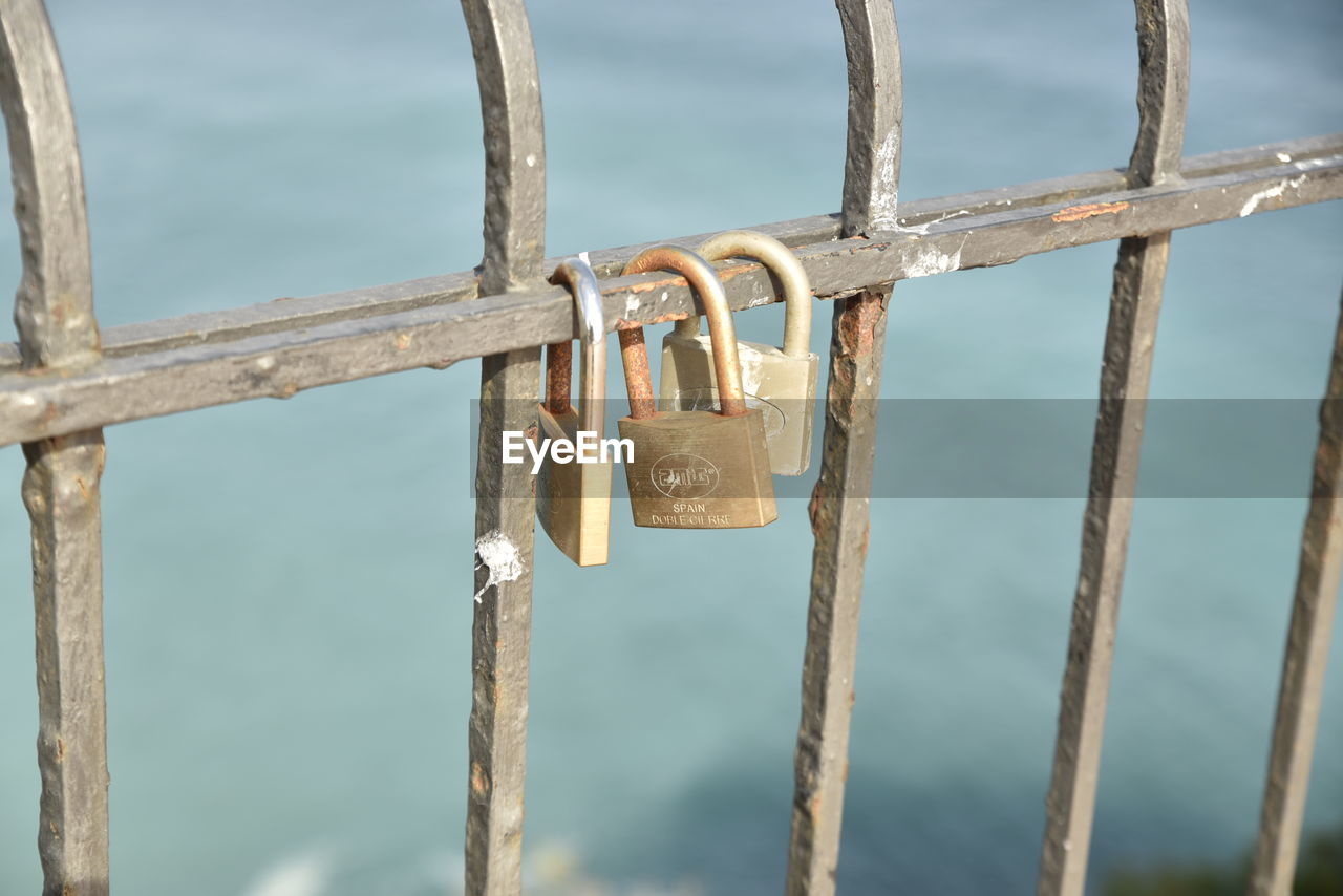 CLOSE-UP OF PADLOCKS HANGING ON RAILING AGAINST SKY