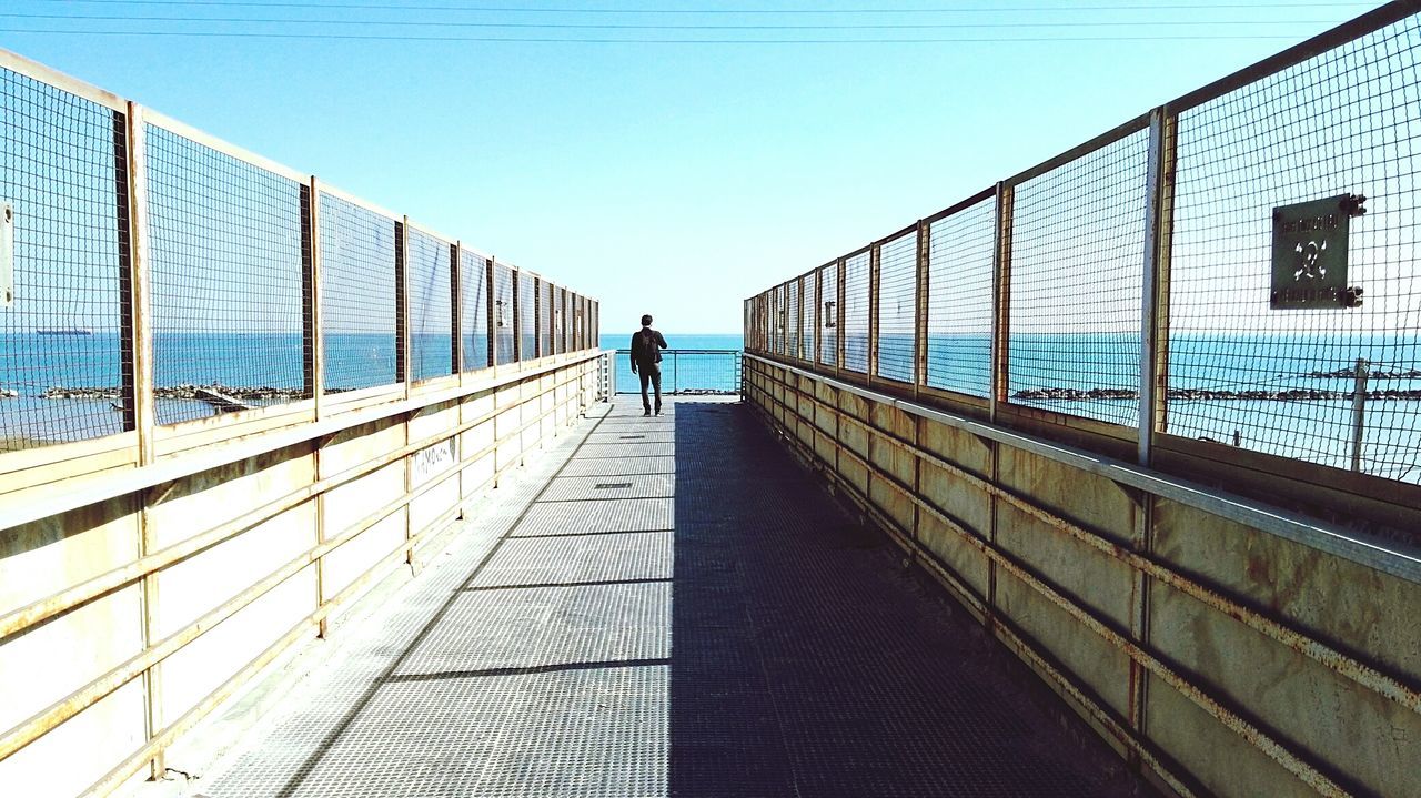 REAR VIEW OF MAN STANDING ON FOOTBRIDGE